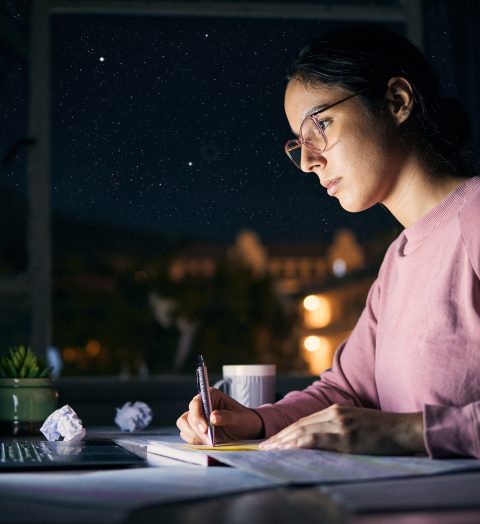 Girl, reading and studying on laptop at night for research, education and internet project. Serious young student, writing notes and learning on computer at dark desk for homework, planning and tech